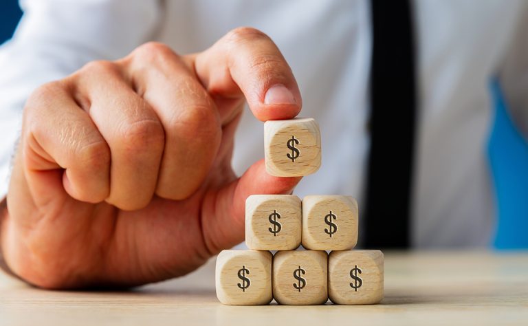 Mão em foco enquanto empilha cubo com cifrão, representando o aumento na rentabilidade da empresa